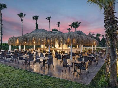 Buitenhotelbar met rieten dak en zitplaatsen bij zonsondergang.