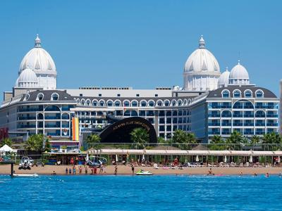 Groot luxe hotel met koepeltorens aan de waterkant onder een heldere blauwe lucht.