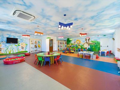 Lichte, kleurrijke speelruimte met muurschilderingen, tafels en speelgoed in een hotel of vakantieomgeving.