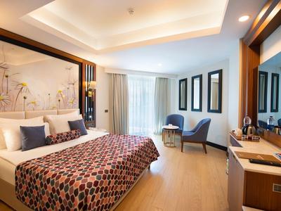 Lichte hotelkamer met een groot bed, bedsprei met patroon, zithoek en houten vloer.