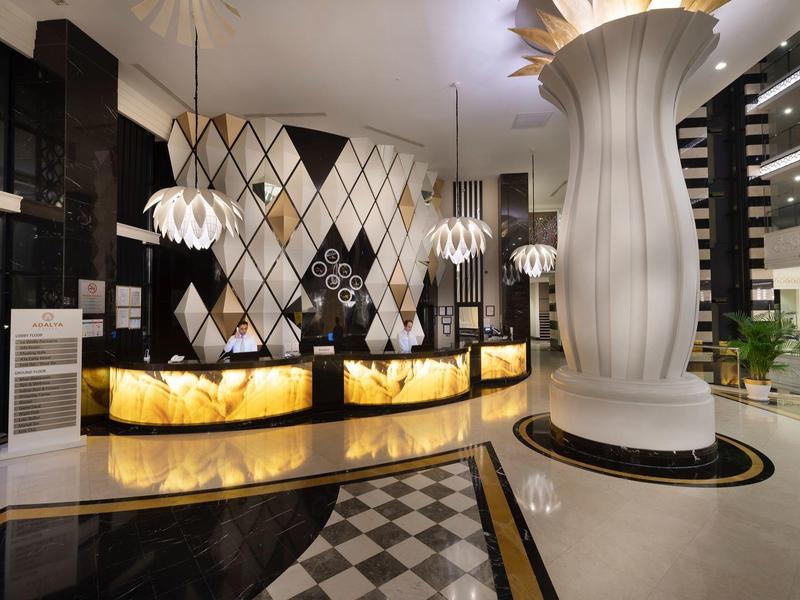 Luxe hotellobby met verlichte gebogen balies, geometrisch wandontwerp en hanglampen.