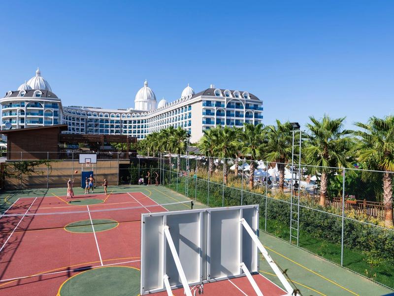 Modern hotel met koepeldaken naast een omheind buitenbasketbalveld en palmbomen.