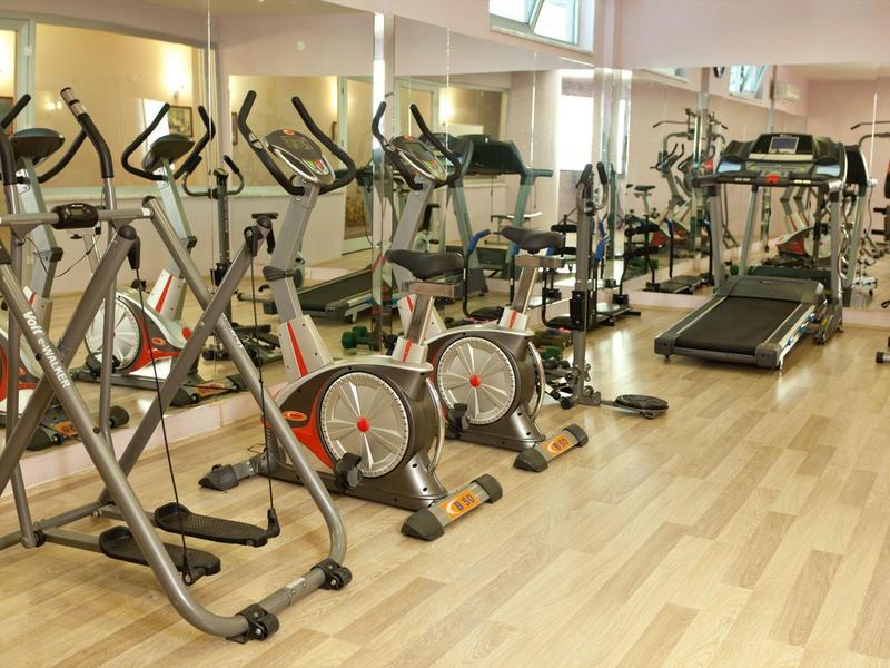 Fitnessruimte met hometrainers, loopbanden en spiegelwanden op houten vloer.