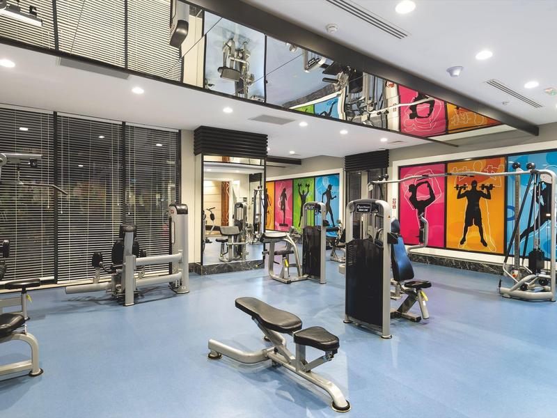 Moderne fitnessruimte met apparaten, blauwe vloer en kleurrijke muurschilderingen.