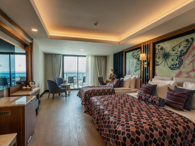 Moderne hotelkamer met twee bedden, balkon, uitzicht op zee en warme sfeerverlichting.