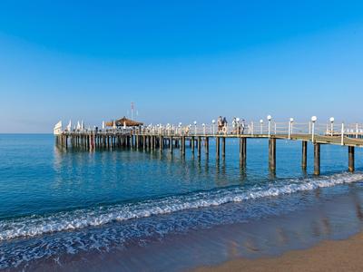 Dřevěné molo se táhne přes klidné moře pod modrou oblohou a písečnou pláží.
