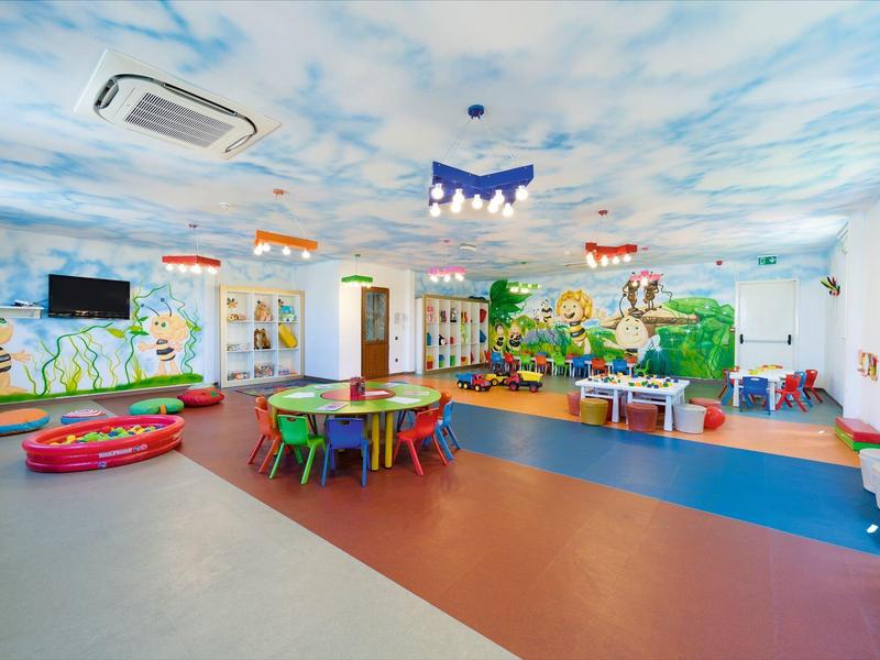 Barevná herna pro děti s stolky, židlemi a veselými nástěnnými malbami.