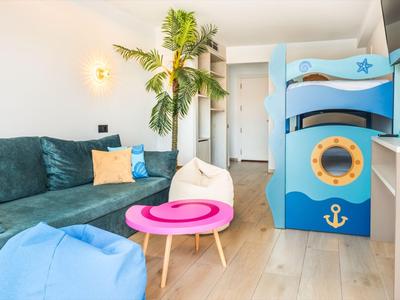 Heller Hotelzimmer mit blauem Kinderspielbett, Sofa, Sitzsäcken und kleinen Tischen.