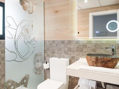 Modernes Hotelbadezimmer mit Glasdusche, Holzdetails und Waschbecken aus Naturstein.