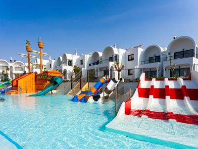 Großer Hotelpool mit bunten Wasserrutschen und weißem Gebäude im Hintergrund unter klarem Himmel.