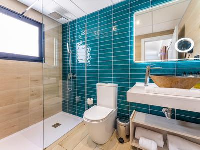 Modernes Badezimmer mit blauen Wandfliesen, weißem Waschbecken, Toilette und großer Dusche.