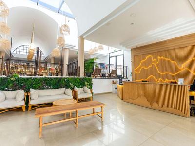 Helle Hotel-Lobby mit Holzrezeption, modernen Sitzmöbeln und großer Glasdecke