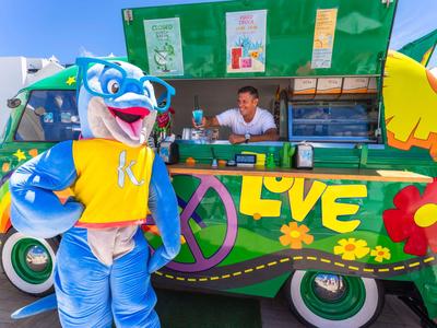 Bunte Foodtruck-Szene mit Delfin-Maskottchen und lächelndem Mann
