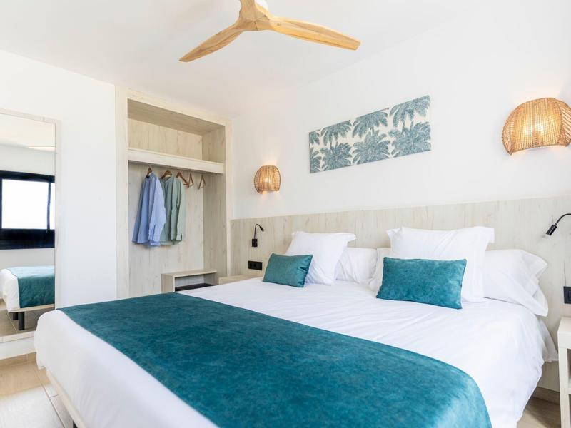 Modernes Schlafzimmer mit großem Doppelbett, hellen Wänden, blauen Akzenten und Deckenventilator.