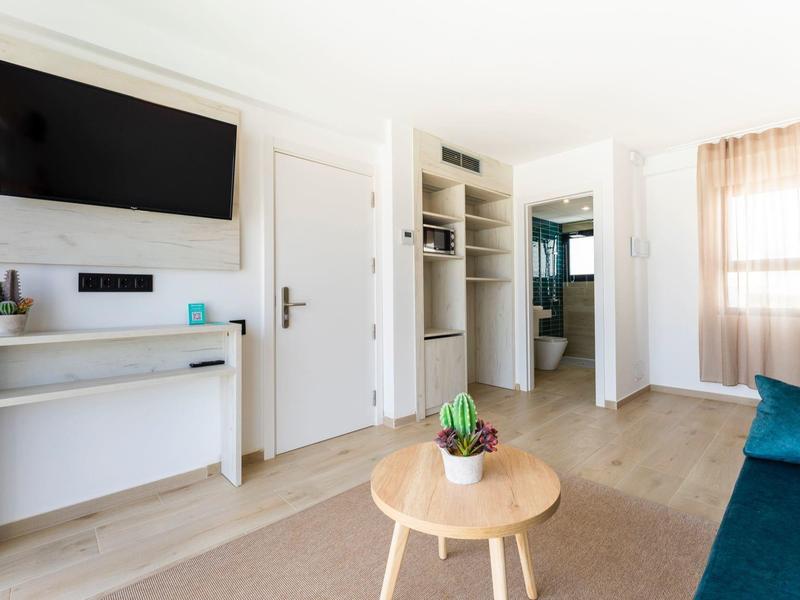 Helles Wohnzimmer mit hellen Holzboden, weißem Wandregal, Fernseher und kleinem runden Holztisch.