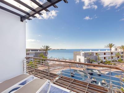 Vue depuis un balcon avec des transats sur une piscine et la mer sous un ciel clair.