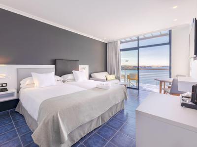 Chambre d'hôtel lumineuse avec deux lits, porte terrasse et vue sur la mer