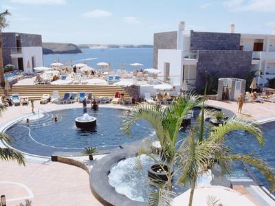 Espace piscine d'hôtel avec fontaine, transats et vue sur la mer.
