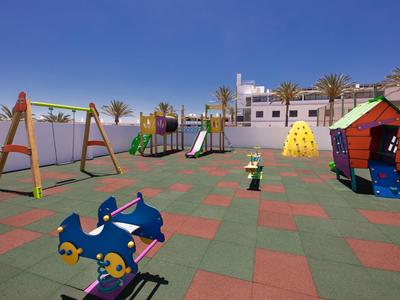 Aire de jeux colorée pour enfants avec balançoires, toboggans et maisonnette sous ciel bleu.