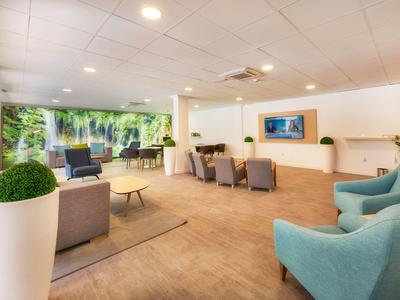 Espace lounge et attente d'hôtel moderne avec fauteuils, sièges et grande baie vitrée donnant sur la nature.