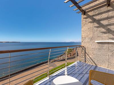 Balcon avec chaise, table, vue sur la mer et ciel dégagé.
