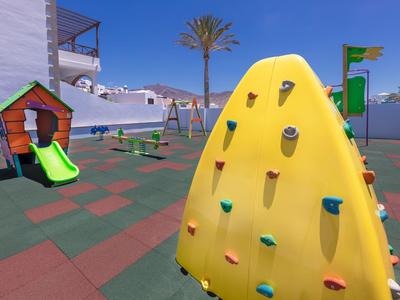 Aire de jeux pour enfants avec mur d'escalade, toboggan et balançoires sur la terrasse de l'hôtel.