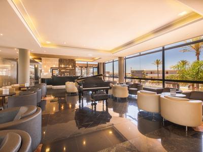 Spacieuse salle de l'hôtel avec piano, fauteuils confortables et fenêtres panoramiques offrant une vue.