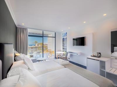 Chambre d'hôtel moderne avec deux lits, grande fenêtre et télévision murale.