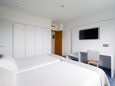 Chambre d'hôtel lumineuse avec deux lits, grands placards muraux et télévision au-dessus d'un bureau.