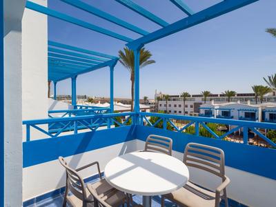 Balcon avec rambarde bleue, table ronde blanche et chaises avec vue sur l'hôtel et les palmiers.