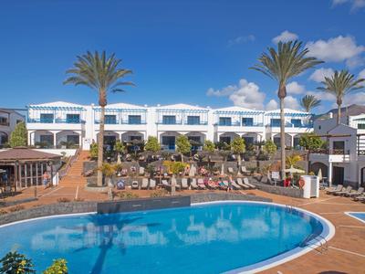 Complexe hôtelier avec piscine, chaises longues et palmiers sous un ciel bleu clair