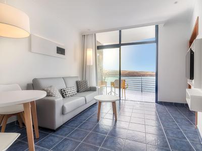 Salon moderne avec canapé gris, petite table et accès au balcon avec vue sur la mer.