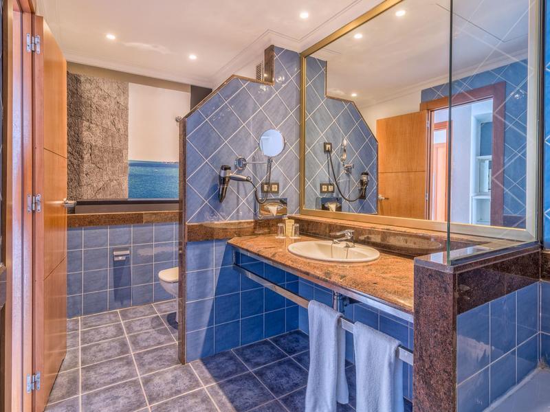 Salle de bain moderne avec carrelage bleu, grand miroir et accents en bois.