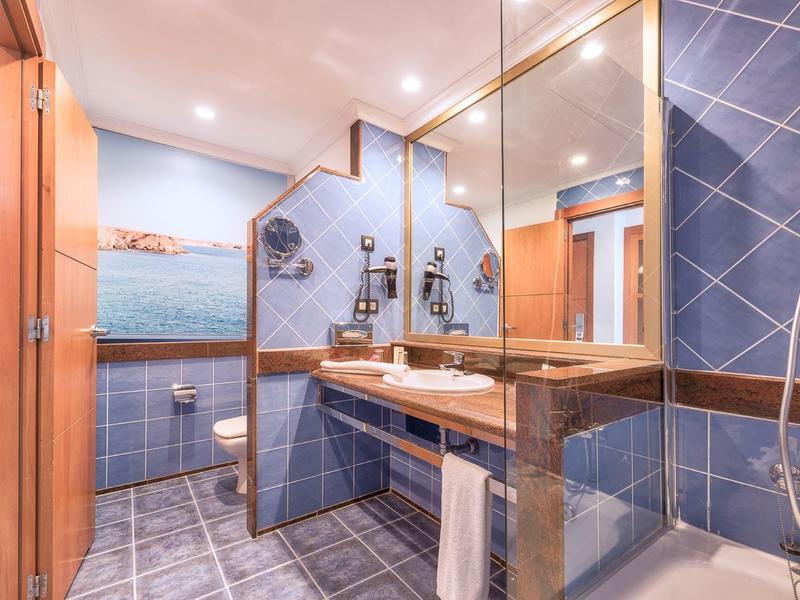 Salle de bain moderne avec carrelage bleu, doubles lavabos et grand mur miroir.