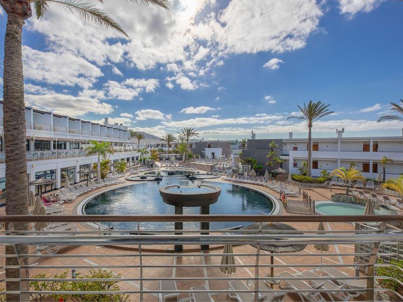 Complexe hôtelier moderne avec piscine, palmiers et espaces assis sous un ciel bleu