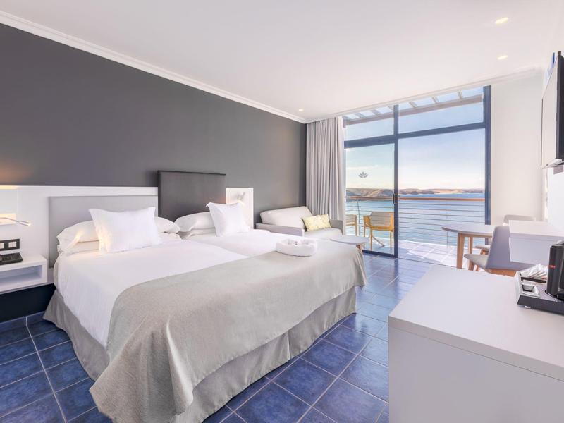 Chambre d'hôtel lumineuse avec deux lits, porte terrasse et vue sur la mer