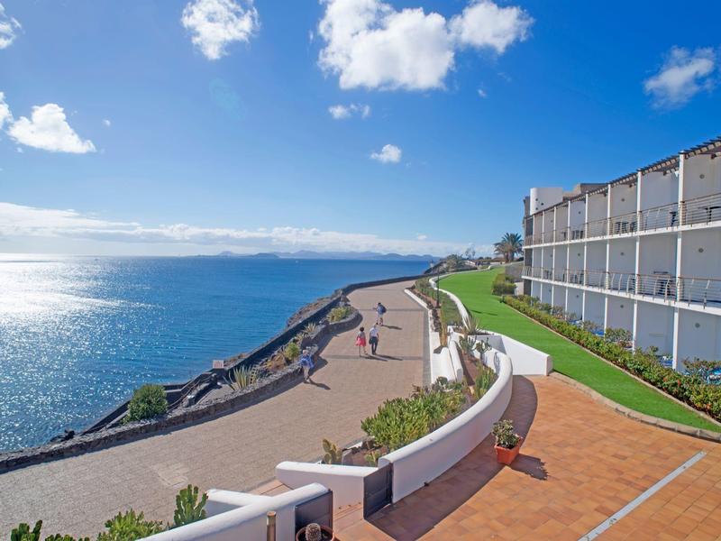 Promenade côtière dégagée avec vue sur la mer, chemin de promenade et bâtiments modernes.