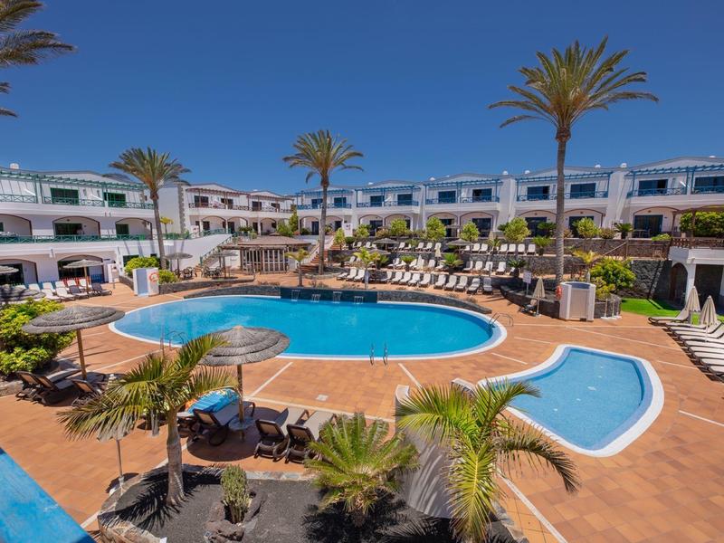 Piscine ronde d'hôtel avec chaises longues et palmiers sous un ciel dégagé.