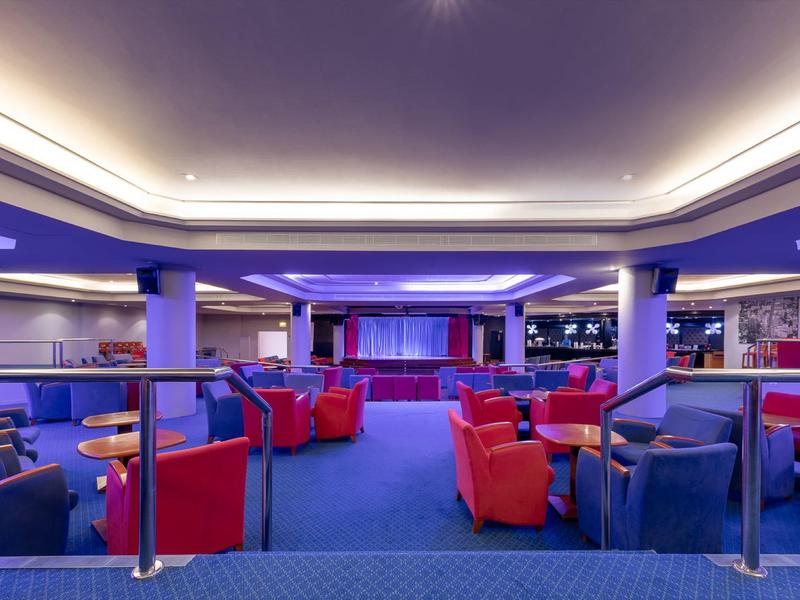 Salon moderne avec tapis bleus et fauteuils rouges dans un bar d'hôtel.