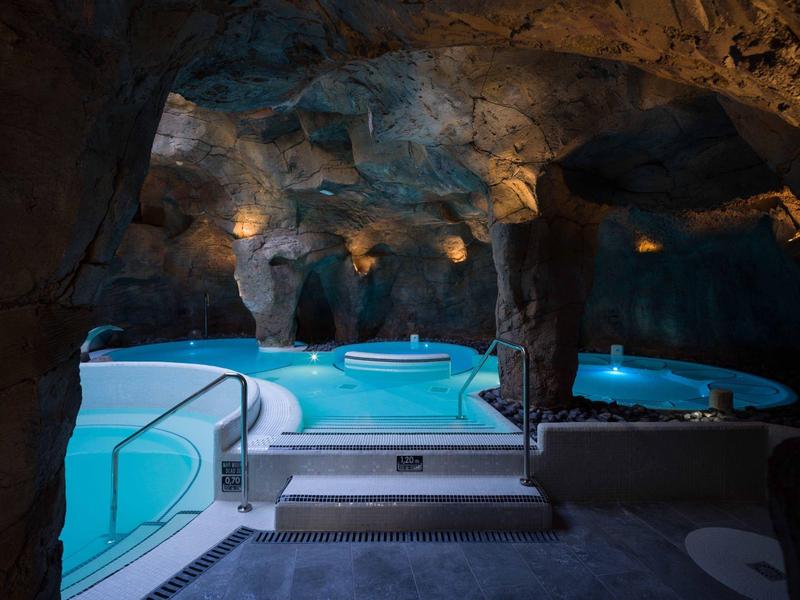 Piscine intérieure dans une grotte naturelle avec eau éclairée et espace jacuzzi.