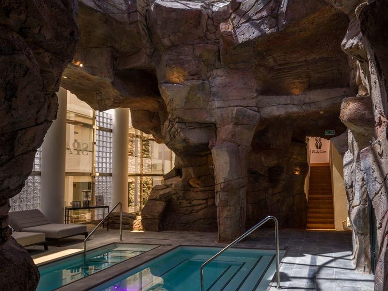 Piscine chauffée dans un environnement de spa rocheux avec puits de lumière en verre.