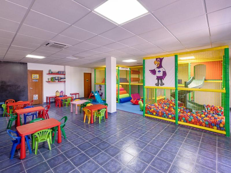Salle de jeux colorée pour enfants avec tables, chaises et piscine à balles dans l'hôtel.