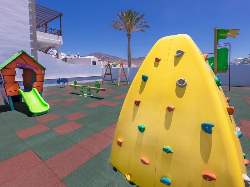 Aire de jeux pour enfants avec mur d'escalade, toboggan et balançoires sur la terrasse de l'hôtel.