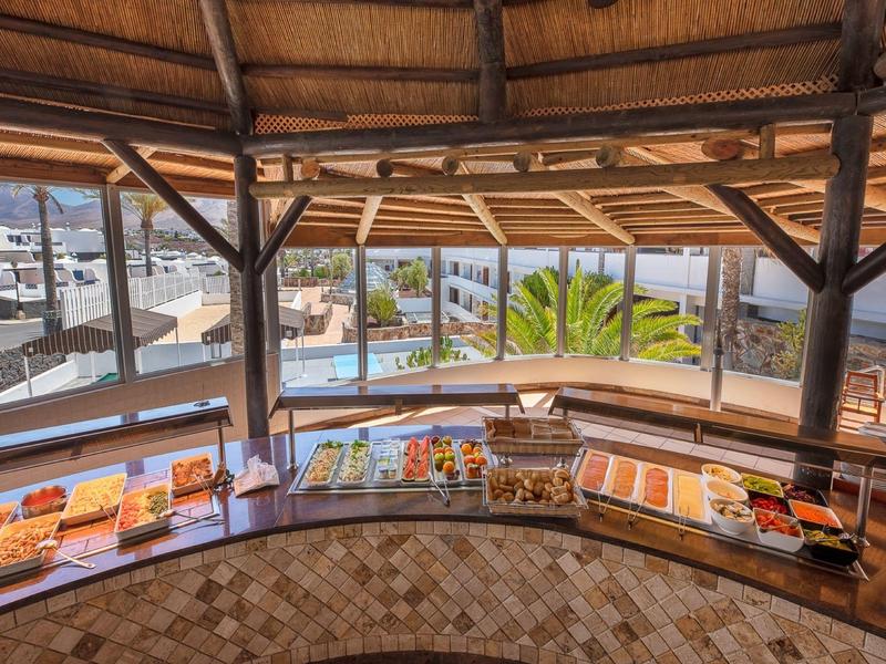 Buffet avec divers aliments sous un espace couvert avec vue sur une piscine et des palmiers.