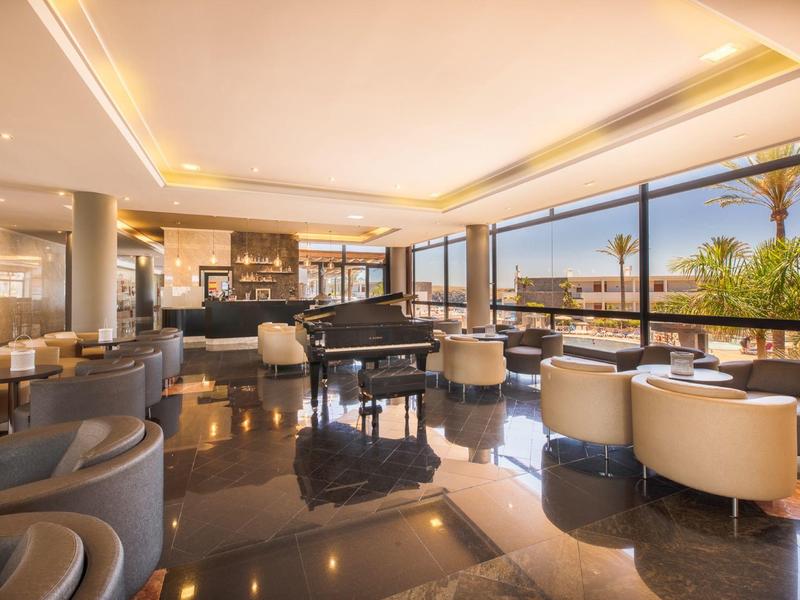 Spacieuse salle de l'hôtel avec piano, fauteuils confortables et fenêtres panoramiques offrant une vue.