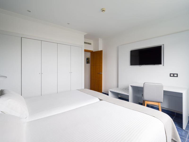 Chambre d'hôtel lumineuse avec deux lits, grands placards muraux et télévision au-dessus d'un bureau.