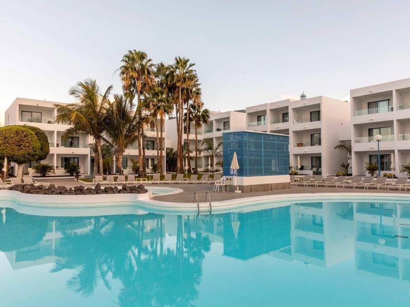 Modern hotel complex with clear pool and palm trees in courtyard during daylight.
