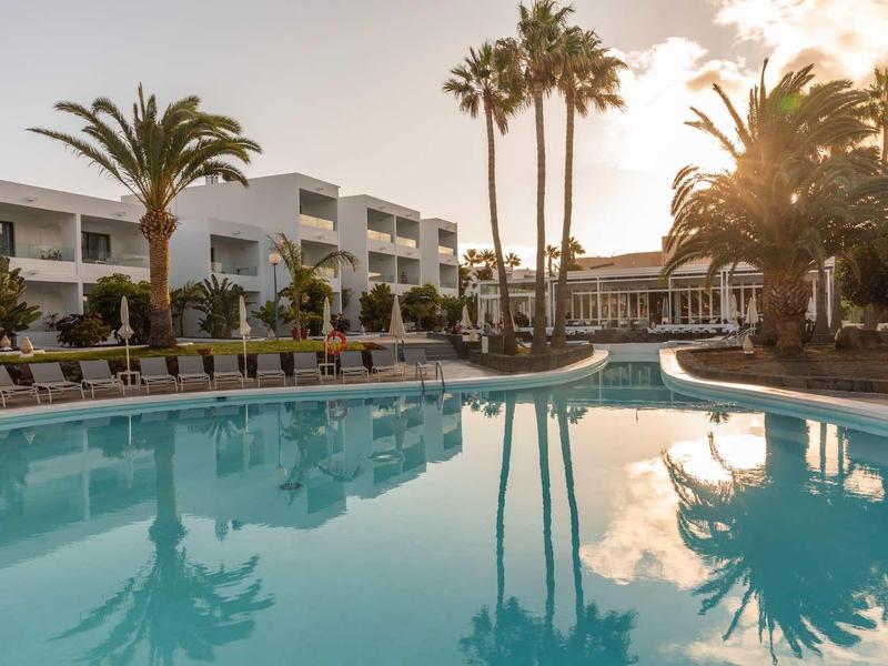 A hotel pool with sun loungers and palm trees at sunset.