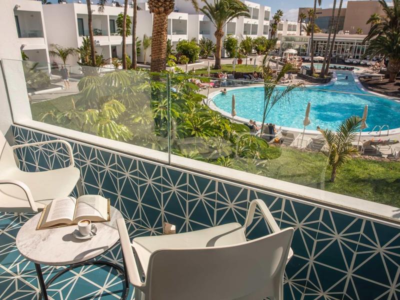 View from a balcony with chairs and table overlooking a hotel pool and garden area.