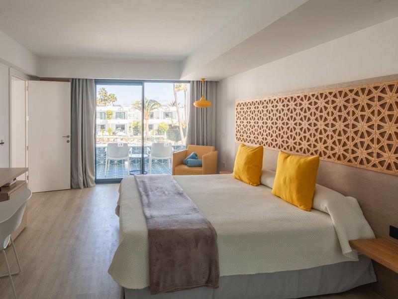 Modern hotel room with double bed, yellow pillows, and terrace overlooking the neighborhood.